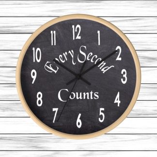 A round wall clock with a wooden frame and black chalkboard face displays white numbers. The text "Every Second Counts" is written diagonally across the center. The background is light wooden planks, creating a rustic feel.