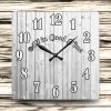 Square wooden clock with large black numbers and the phrase "All in Good Time" across the center. Background features horizontal wooden planks.