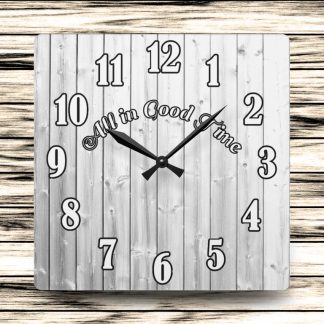 Square wooden clock with large black numbers and the phrase "All in Good Time" across the center. Background features horizontal wooden planks.