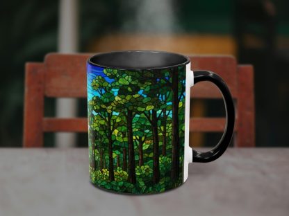 A steaming black mug sits on a table, featuring a vibrant stained-glass forest design with lush green trees and a blue sky, set against a blurred chair.