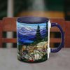 A steaming mug with a stained glass-style design depicting a scenic mountain landscape with trees. The background features a blurred wooden chair.