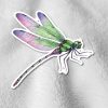A colorful dragonfly sticker with green and pink wings is placed on a textured, light gray fabric, creating a whimsical and vibrant contrast.
