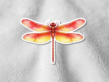 Sticker of a vibrant red and orange dragonfly with detailed wings on a soft, textured gray surface. The image conveys a sense of warmth and lightness.