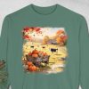 Green sweatshirt with an autumn farm scene. A wagon of pumpkins sits in a field with cows, a barn, and vibrant fall foliage. Cozy and rustic theme.