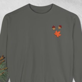 Dark gray sweatshirt on textured gray background. Decorative fall-themed patches: two acorns and a maple leaf in red and orange tones add a seasonal touch.