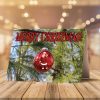 A Christmas card on a wooden table features a Santa ornament on the cover with "Merry Christmas!" text. Inside, there are red tree shapes and festive wishes. Two candy canes and pine sprigs add holiday cheer.