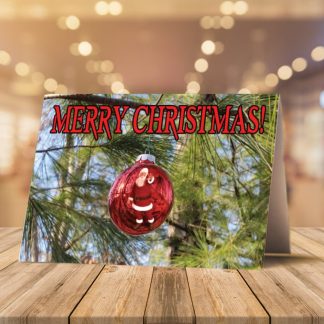 A Christmas card on a wooden table features a Santa ornament on the cover with "Merry Christmas!" text. Inside, there are red tree shapes and festive wishes. Two candy canes and pine sprigs add holiday cheer.