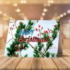 Christmas card on a wooden table. Open card with bells and holiday message. Closed card with "Merry Christmas," berries, and evergreen branches. Candy canes and pine sprigs add festive cheer.