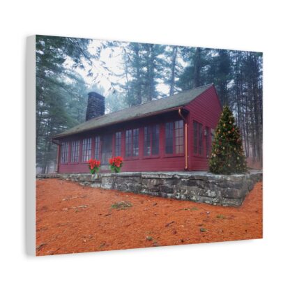 Canvas wall art print of a red cabin with numerous windows and a chimney stands amidst a forest. A decorated Christmas tree is on the right, with vibrant poinsettias below front windows.
