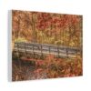 A wooden bridge crosses a serene creek surrounded by lush autumn foliage in shades of orange, red, and yellow. The scene conveys a peaceful, natural beauty.