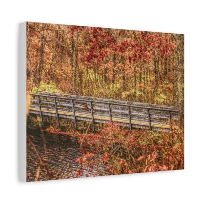 A wooden bridge crosses a serene creek surrounded by lush autumn foliage in shades of orange, red, and yellow. The scene conveys a peaceful, natural beauty.
