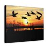Silhouette of geese flying at sunset over reeds, with the sun setting below the horizon. Warm orange sky creates a peaceful and serene ambiance on canvas wall art.