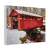 A red covered bridge stands over a snowy creek with falling snowflakes. Bare trees frame the scene. A sense of calm and nostalgia in winter printed on canvas wall art.