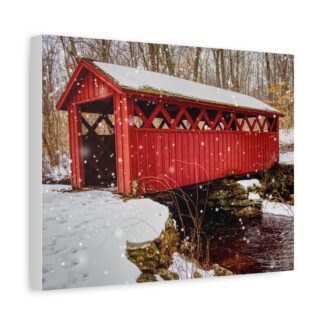 A red covered bridge stands over a snowy creek with falling snowflakes. Bare trees frame the scene. A sense of calm and nostalgia in winter printed on canvas wall art.