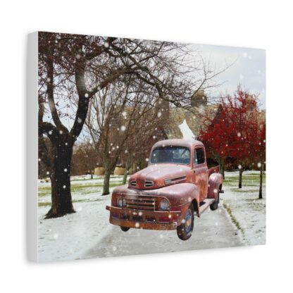 A vintage red truck is parked on a snowy path between trees, with a backdrop of a brick building. Snow gently falls, creating a serene winter scene. Canvas wall art.