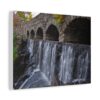 Stone bridge arches over cascading waterfall, surrounded by autumn foliage. Scene conveys a serene and tranquil atmosphere. Canvas wall art.