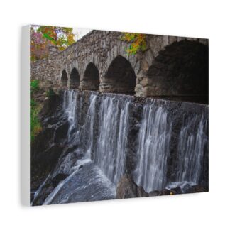 Stone bridge arches over cascading waterfall, surrounded by autumn foliage. Scene conveys a serene and tranquil atmosphere. Canvas wall art.