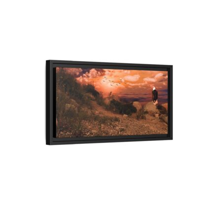Framed canvas artwork of a majestic bald eagle perched on rocks, overlooking a valley and vibrant orange sunset with clouds and flying birds, creating a serene tone.