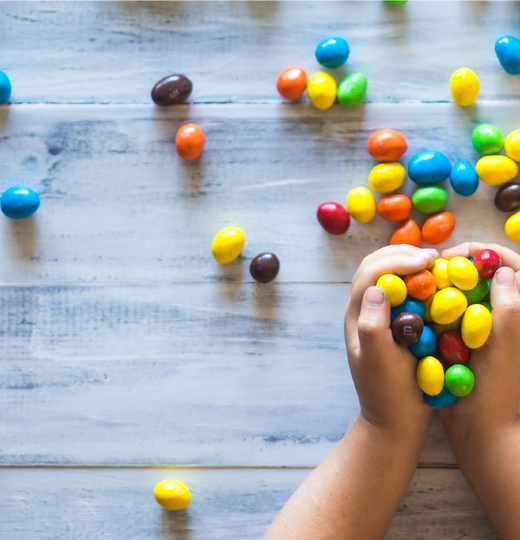 Imagery showing two hands holding an assortment of small candies, and the candies have spilled out onto a wood floor