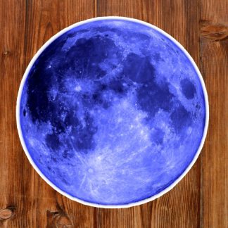Gothic sticker of a round vivid blue moon design sitting on a wooden table, combining a celestial theme with rustic texture, creating a mystical, earthy ambiance.