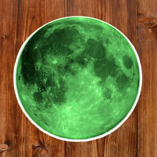 Gothic round sticker of a green moon placed on a rustic wooden surface. The vibrant green tones contrast with the warm, textured wood, creating a mystical atmosphere.