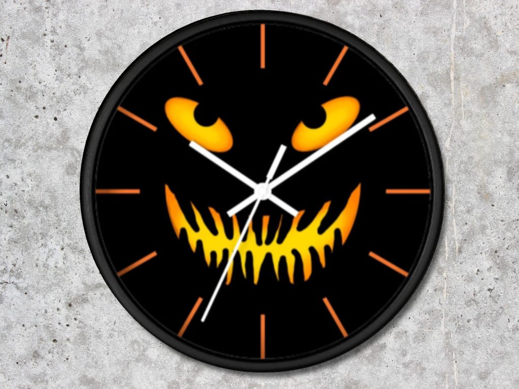 Black clock with a spooky yellow and orange jack-o'-lantern face, featuring glowing eyes and a jagged grin. White hands and orange hour marks. Halloween theme.