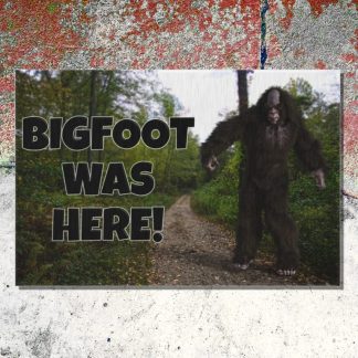 Outdoor welcome mat on a cracked cement floor shows Bigfoot character on a forest path. Bold text reads "BIGFOOT WAS HERE!" conveying a mysterious and playful tone.