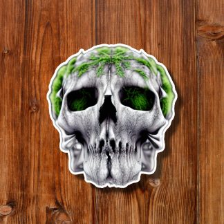 Grim gray skull sticker with glowing green eye sockets and moss-like accents, centered on a warm wooden plank background, creating an eerie mood.