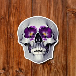 White skull sticker with purple pansy flowers in its eye sockets and nose, centered on a warm wooden plank background; macabre yet artistic.