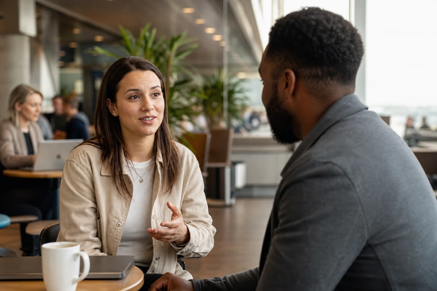 Duas pessoas conversam de forma natural em um espaço que mistura café e área de espera de aeroporto, sugerindo small talk em inglês entre trabalho e viagem.