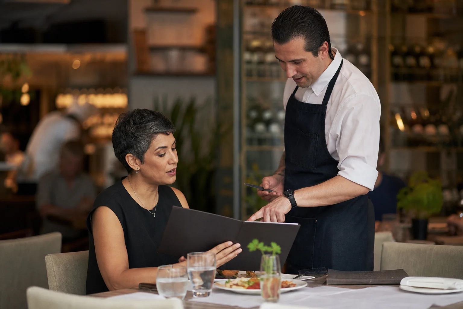 Cliente conversa com atendente enquanto escolhe e adapta o pedido em um restaurante, em cena editorial horizontal.