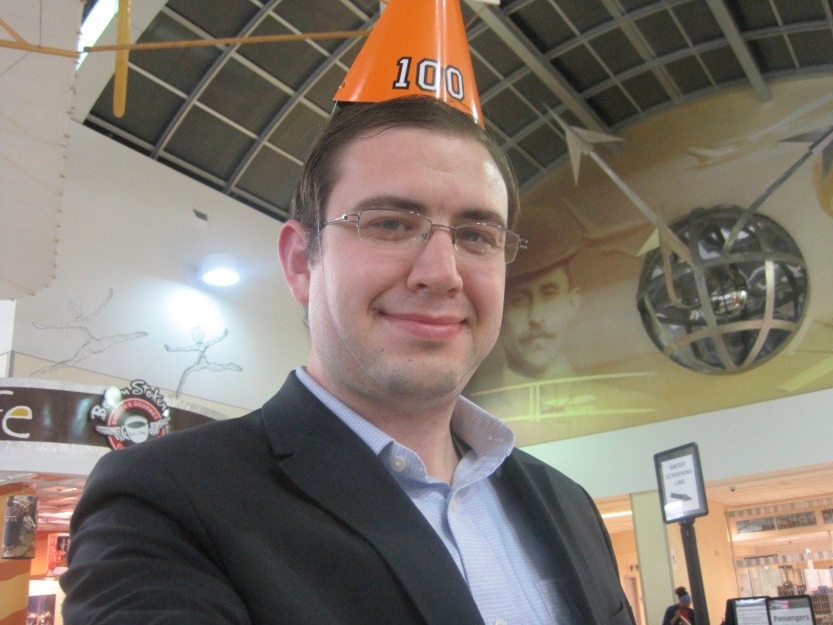Photo of Paul at the Dayton airport wearing a party hat with the number 100 on it