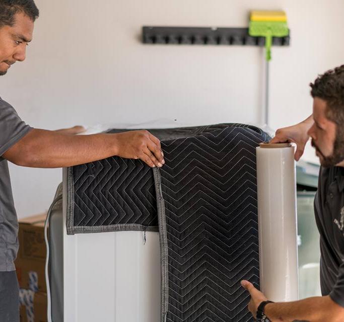 two movers padding and shrink wrapping an item in miami florida