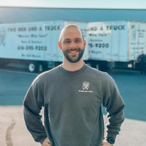 RJ standing in front of a fleet of moving trucks smiling with his hands on his hips