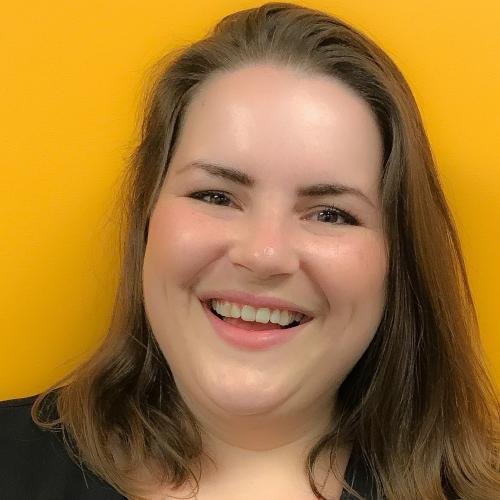 Kristina smiling in front of a yellow wall.