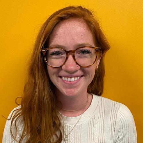 Nicole standing in front of a yellow wall smiling