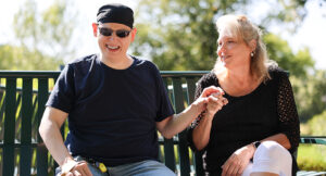 Jason sitting on a park bench with his service provider, Clairanne.