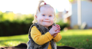 Toddler sitting in a park smiling.