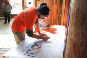 Man in orange shirt signing Summit DD "I Heart Inclusion" banner at Inclusion Days at the Zoo event