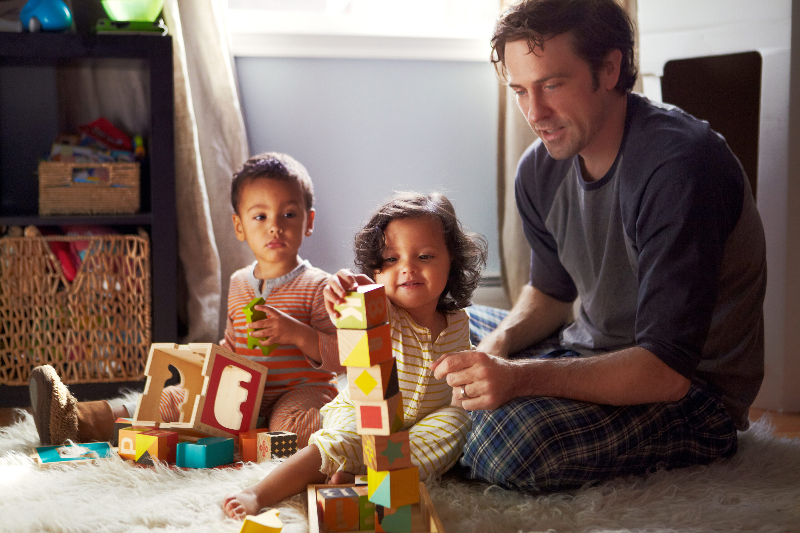 Dad sitting with 2 young children stacking square blocks