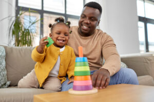 Dad teaching smiling toddler to stack a colorful ring toy
