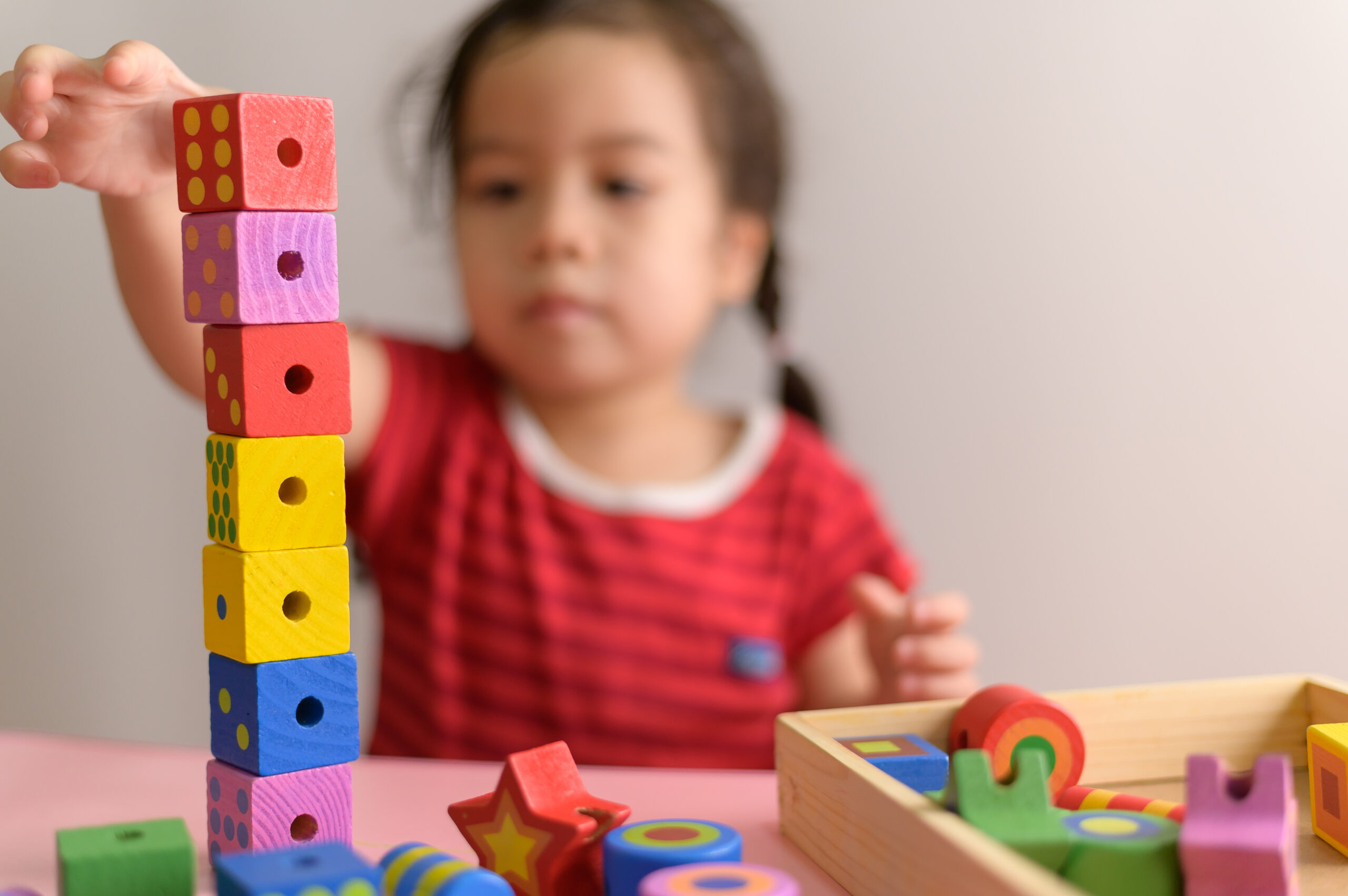 Little curly asian girl enjoy playing with wooden toy blocks isolated on white background. Education and learning Concept.