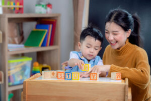 Smiling mom organizing wooden letter blocks with toddler son