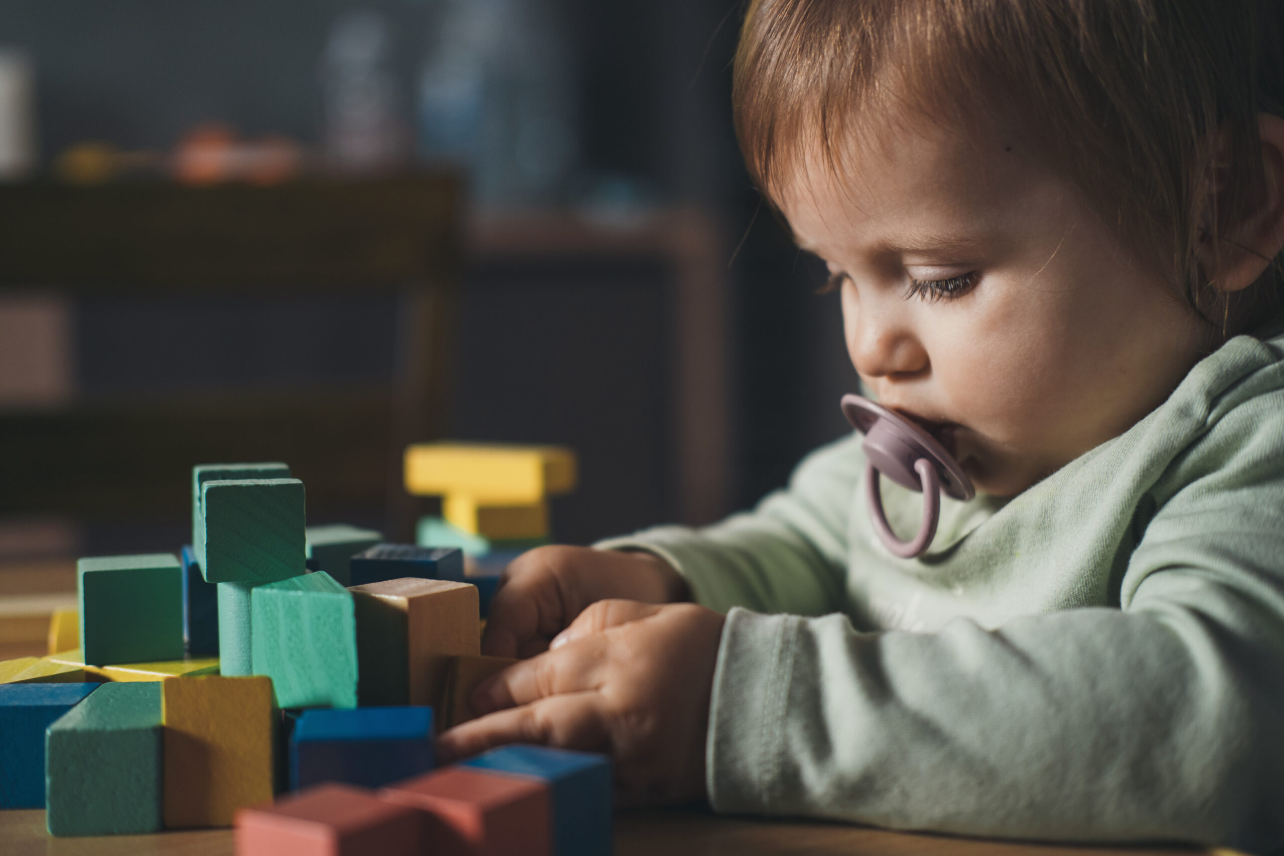 Baby girl playing with colorful toy blocks sitting at table. Building tower of block toys. Children education.