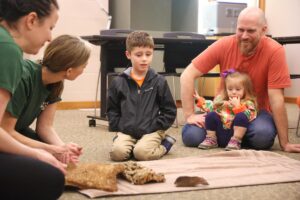 Dad sitting on floor with his 2 young children learning about animals at the Zoo