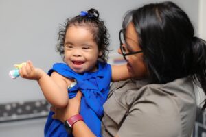 Smiling little girl with Down Syndrome being held by her proud mom
