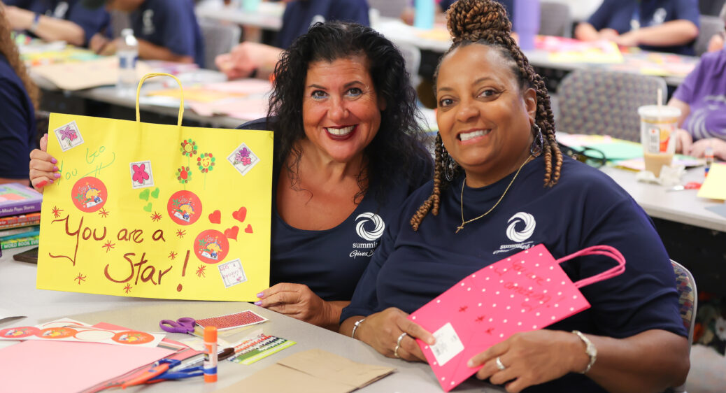 Two women smiling while holding up artwork.