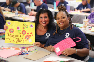 Two women smiling while holding up artwork.
