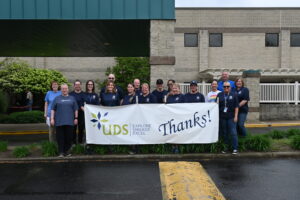 Group of people gathered together outside smiling and holding up United Disabilities sign.