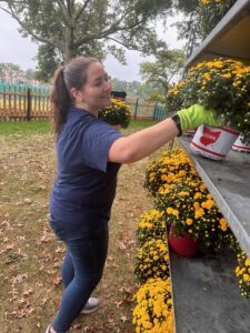 Woman outside smiling while unloading flowers off a cart.